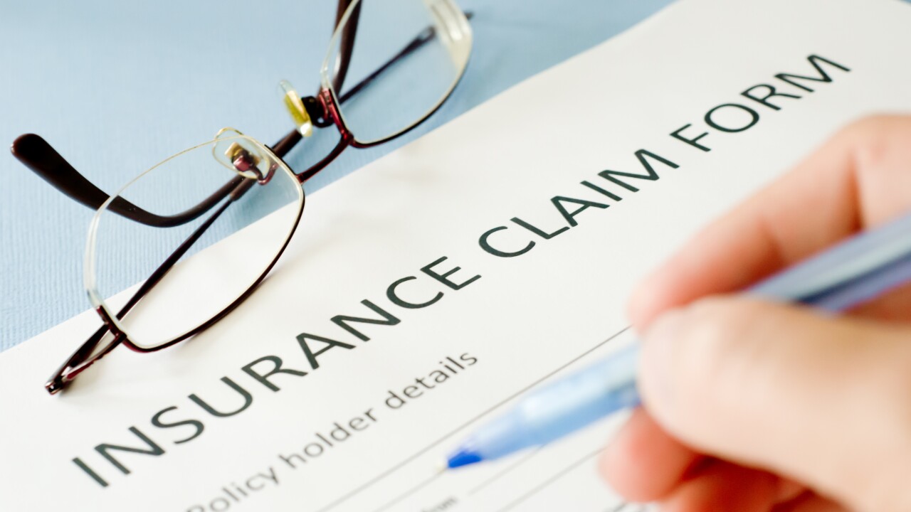 A person filling out an insurance claim form with glasses in frame.