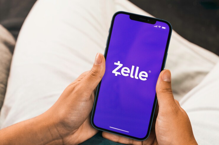Female hand holding a smartphone with Zelle app on the screen.