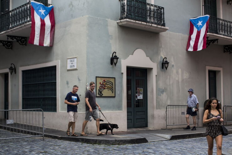 Pedestrians walk under Puerto Rican flags hanging from balconies in San Juan, Puerto Rico, on Sunday, May 1, 2016