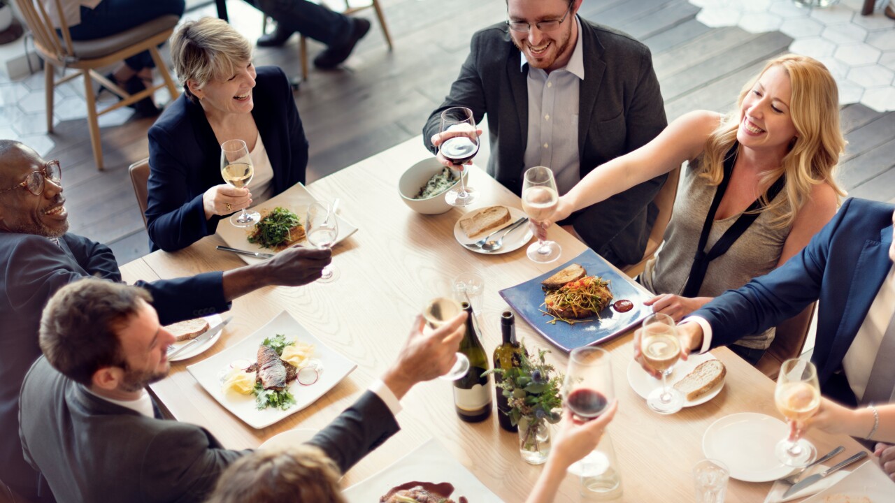 People in business attire hold up wine glasses in a toast over lunch at a restaurant