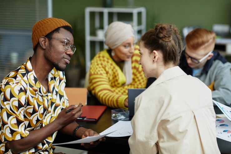 A group of diverse colleagues talk at a table.