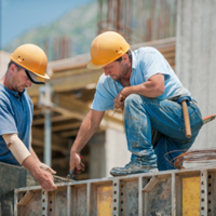Two construction workers collaborating in the installation of concrete formwork frames