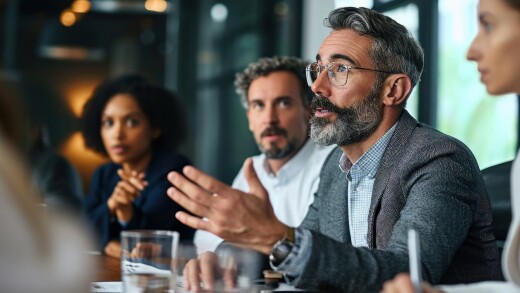 Mature mentor manager speaking at executive team meeting in boardroom.
