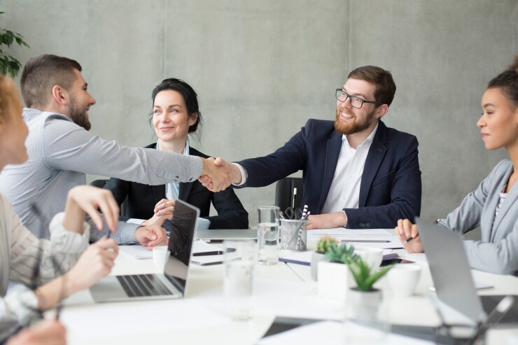 Two men shaking hands during meeting with coworkers