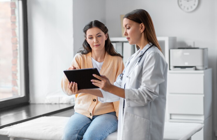 Woman sitting on table at doctor's office, speaking with doctor and looking at tablet
