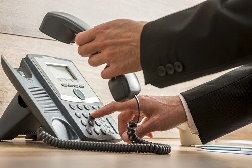 Communication operator dialing a telephone number while holding a handset on a classical landline phone about to make a call.