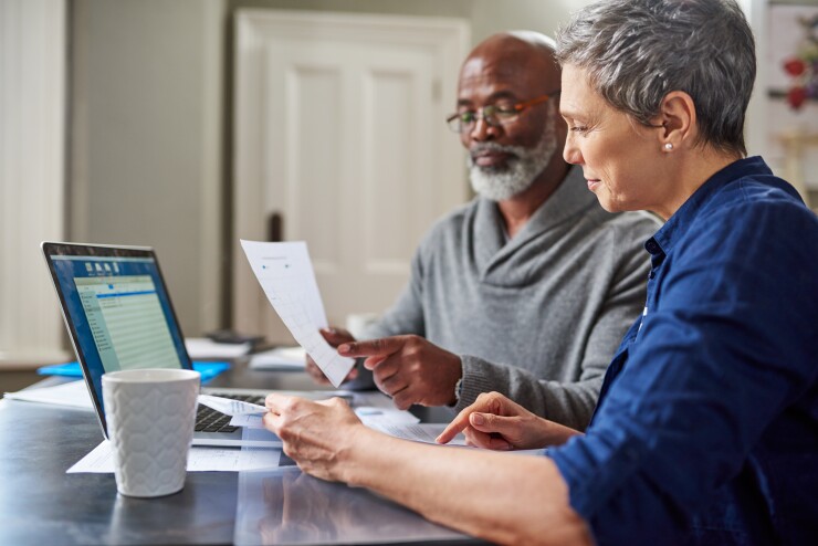 A couple sits around a laptop looking at documents.
