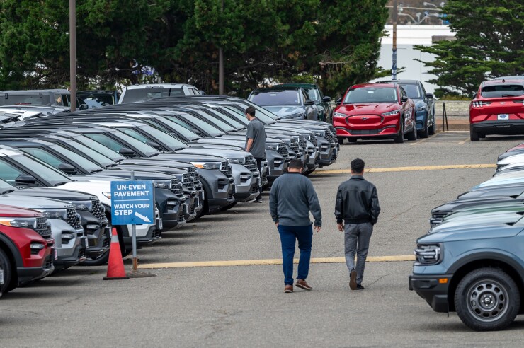Two people walking between rows of used cars.