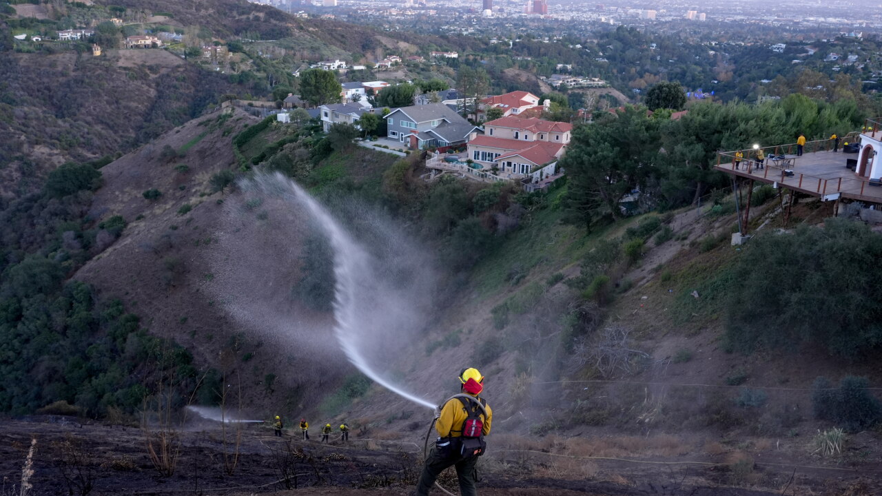 A firefighter spraying water from a hose in the aftermath of the Palisades Fire in the Mandeville Canyon area of Los Angeles in 2025.