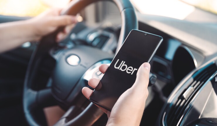 You see one hand on a steering wheel and another hand holding a phone that says "Uber" on it.
