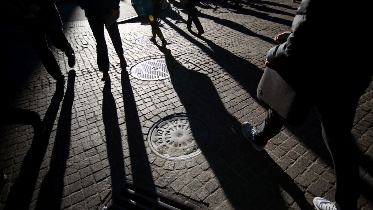 People's feet walking away on dark brick road, shadows behind them