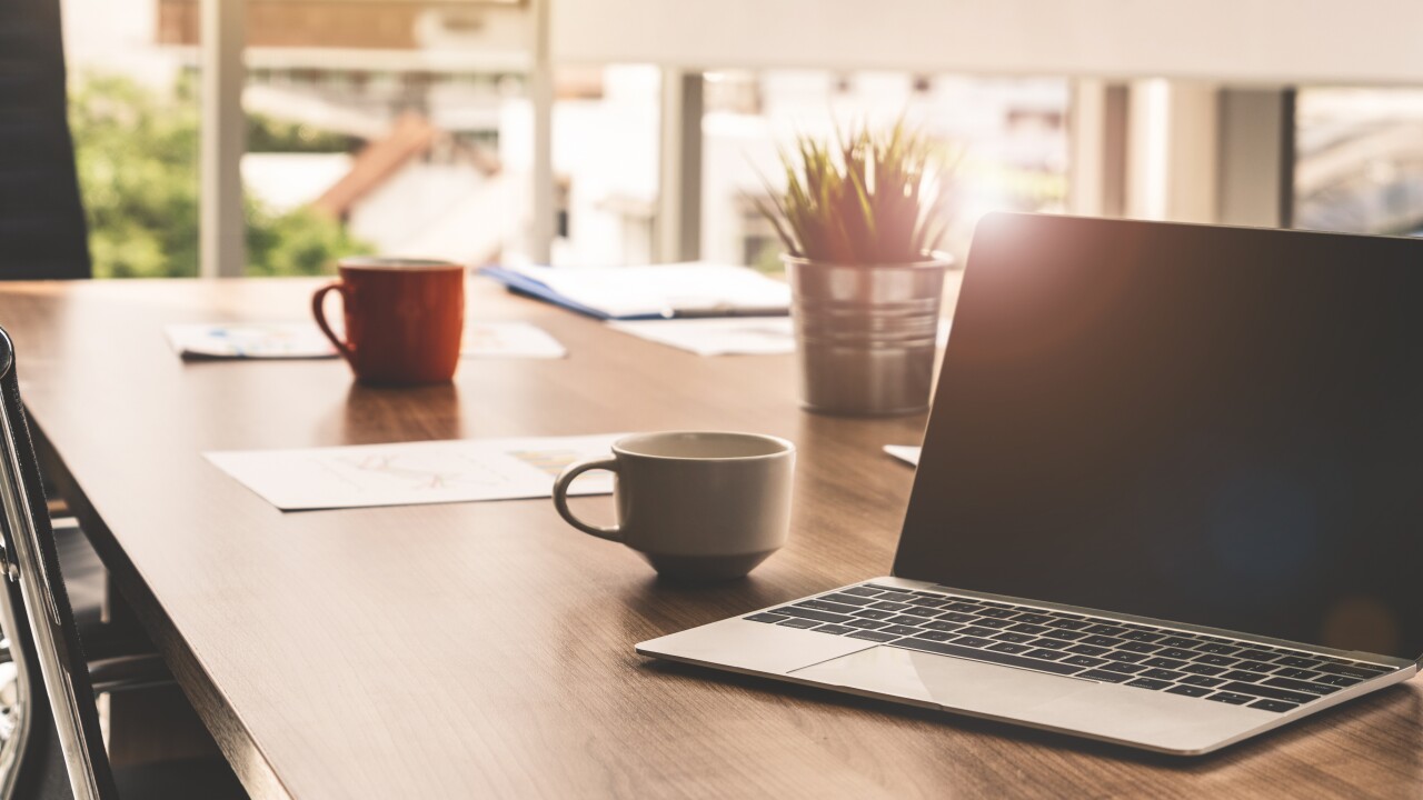 A laptop on a table with a mug and some papers