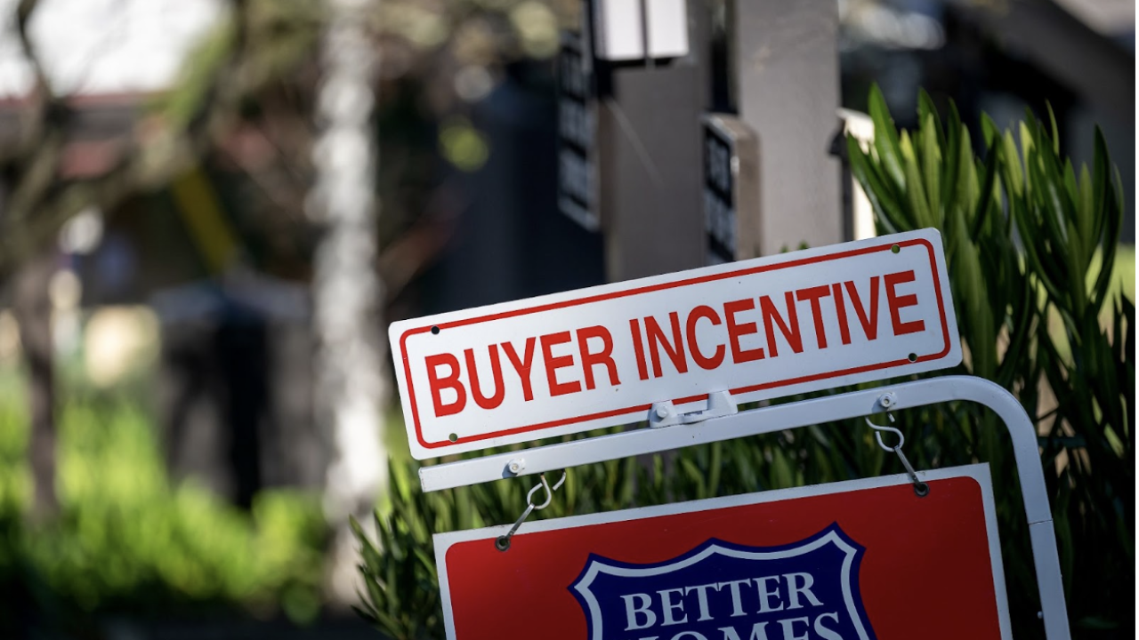 A picture of a for-sale sign outside a house with another sign that says "buyer incentive" on top of it.