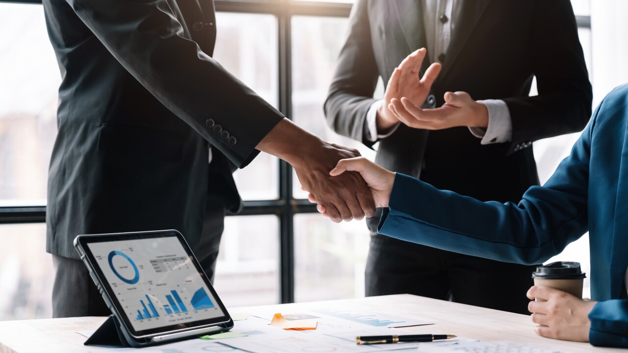 Business people shaking hands over table with tablet and papers