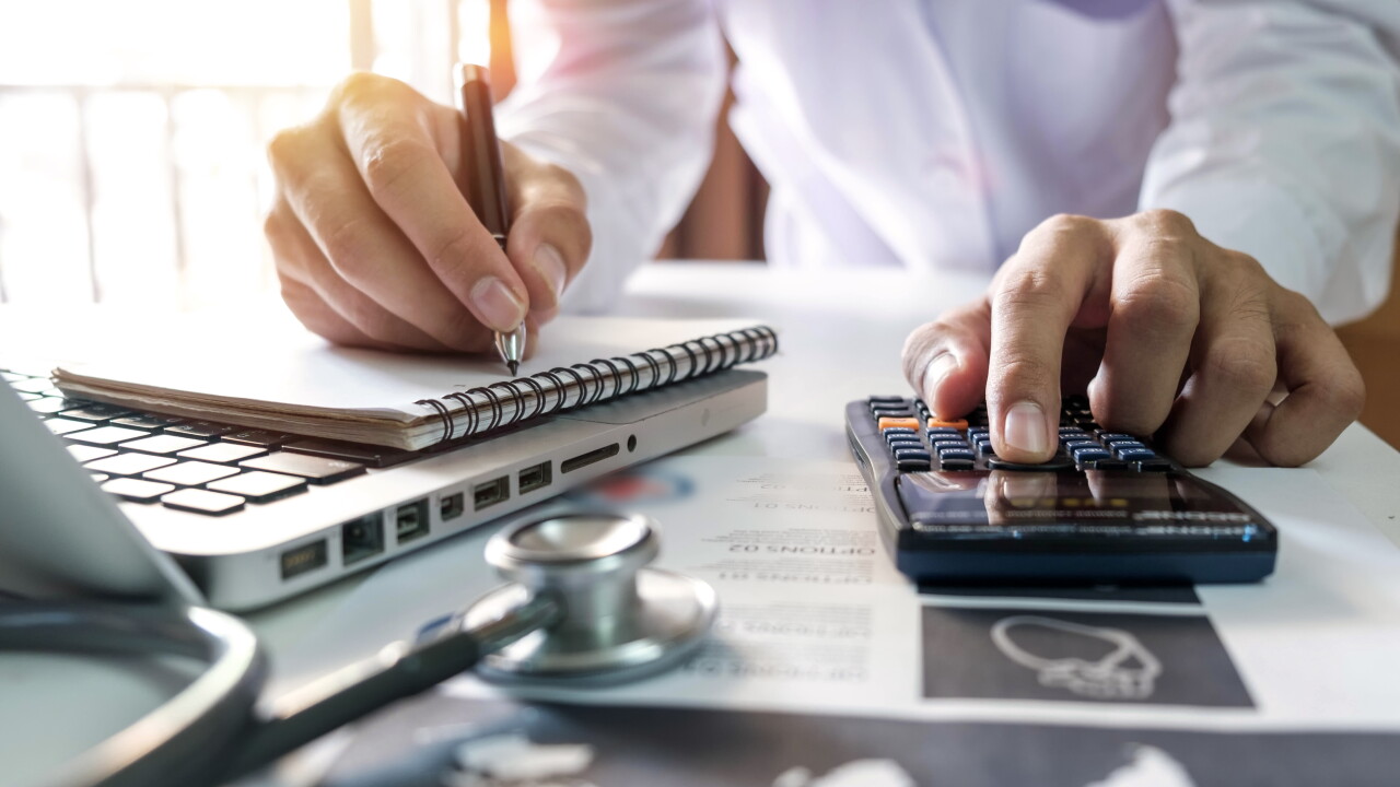 Healthcare costs and fees concept.Hand of smart doctor used a calculator and smartphone for medical costs at modern hospital in sun light.