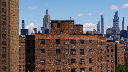Brown brick apartment buildings in NYC with the Empire State Building and Midtown skyline under a clear blue sky.