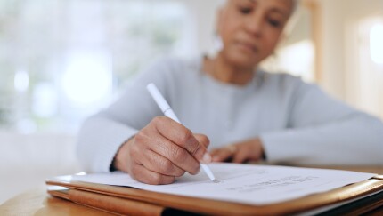 A woman holding a pen and writing on a sheet of paper.