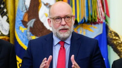 Russell Vought speaks in front of a set of flags.