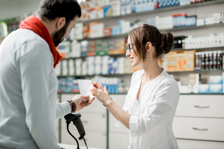 A female pharmacist points to a male customer's prescription at the counter of the pharmacy