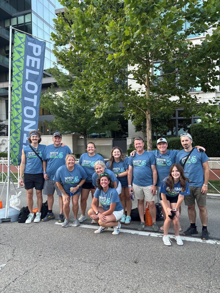 Group of people wearing matching blue shirts stand next to a Peloton banner.