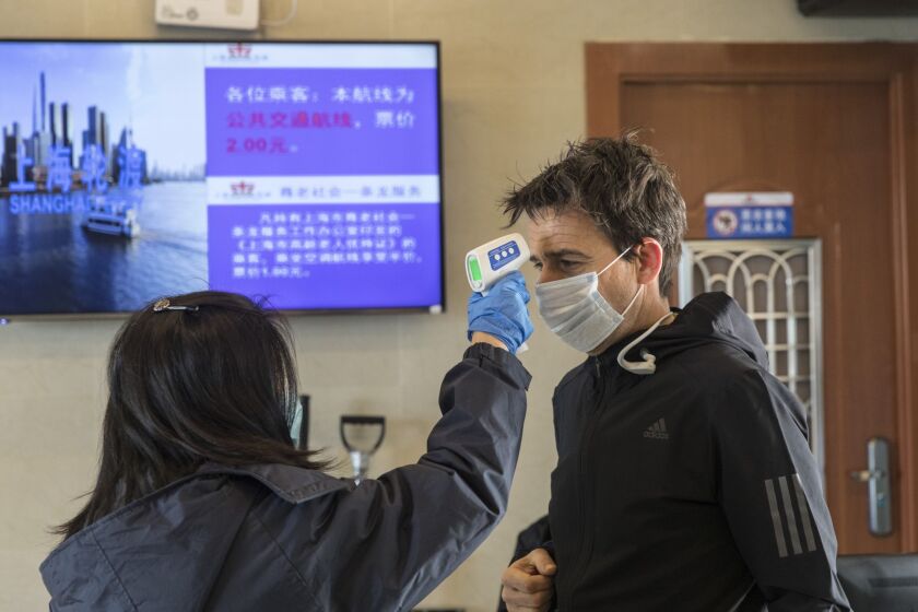 A transit worker takes the temperature of a passenger during a screening at a passenger ferry terminal in Shanghai, China.