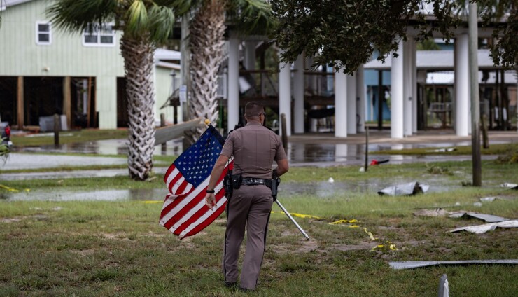 A sheriff's deputy picks up an American flag from debris following Hurricane Idalia in Horseshoe Beach, Florida.