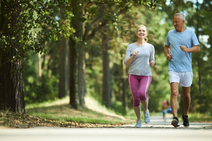An elderly couple jogs at the park.
