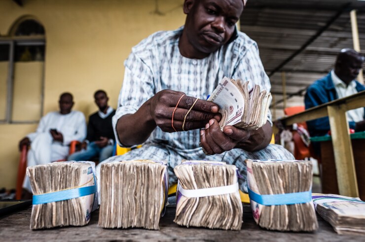A currency dealer uses a mobile phone as he counts bundles of Nigerian naira banknotes for exchange on the 'black market' in Lagos, Nigeria.