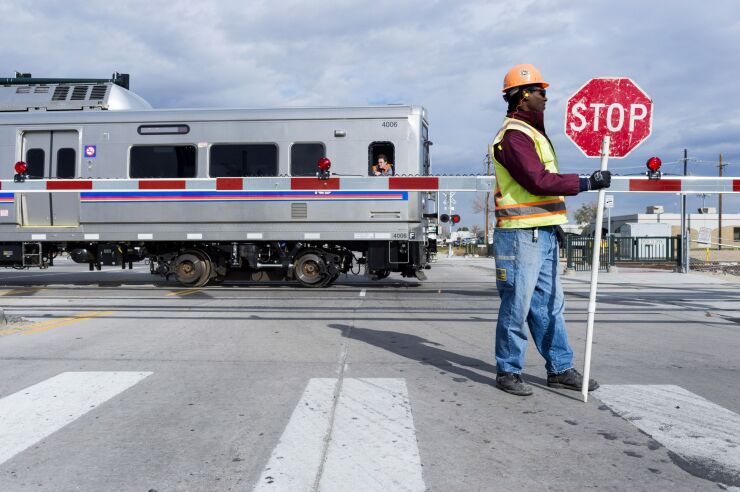 A safety flagger stands watch as an RTD A Line test train traverses a level crossing in Denver, Colorado, U.S., on Monday, Nov. 16, 2015. Level-crossing glitches kept flaggers on duty for more than two years after the line opened to the public.