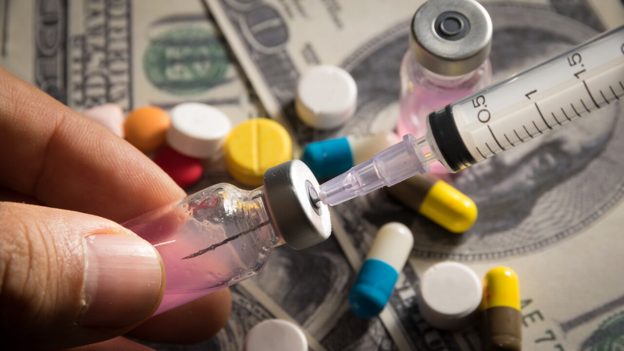 Man's fingers holding small bottle of medicine with syringe; medication; money