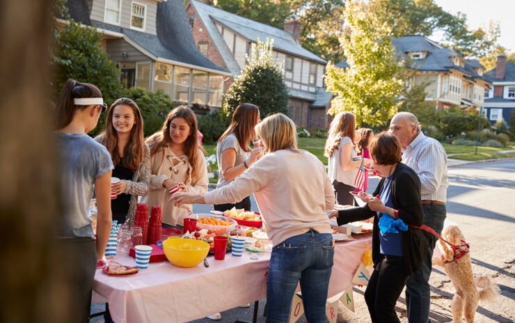 Neighborhood gathering outside on a residential street with people around a table of food.