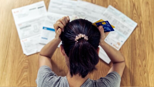 Top view of stressed young woman with hands on head holding credit cards and facing bills