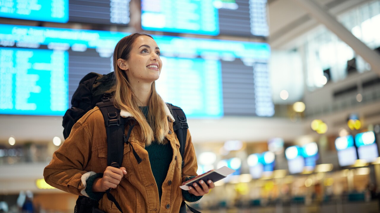Woman standing in airport holding phone with backpack
