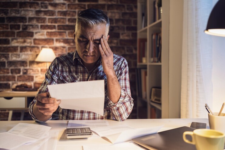 Man with hand on side of head looking at paper with calculator on desk