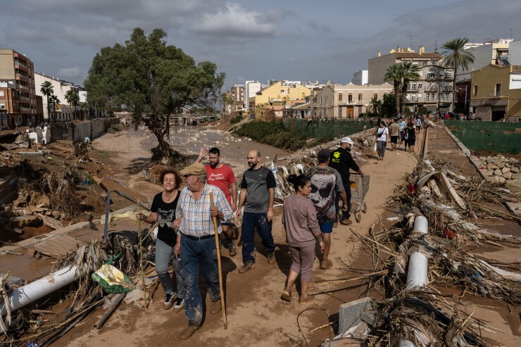People cross a bridge between piles of debris in Paiporta, Spain.