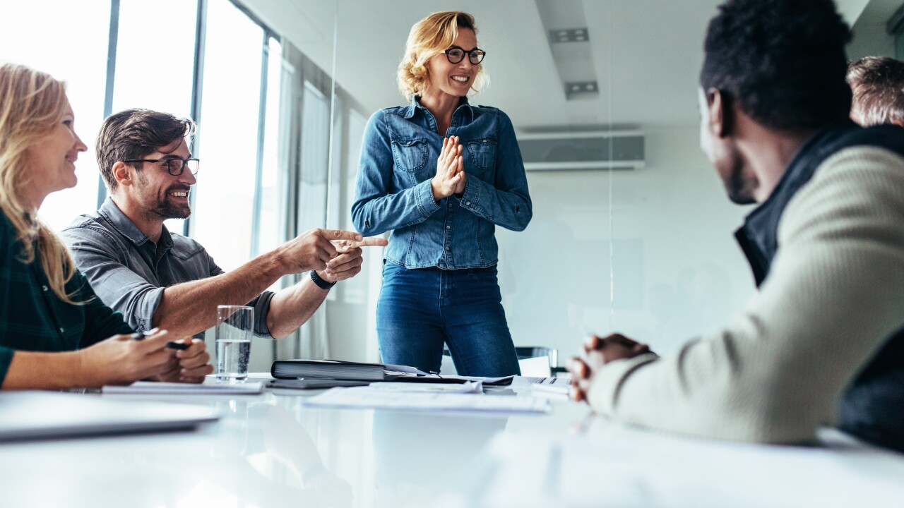 A woman addresses colleagues at the head of a conference table.