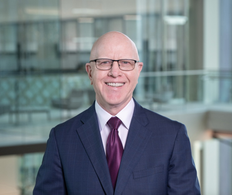 George Gleason of Bank OZK stands in an office building, wearing a suit and tie and smiling.