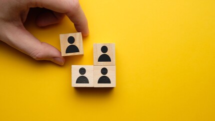 Fired/hired concept - hand holds wooden block with abstract worker on a yellow background.