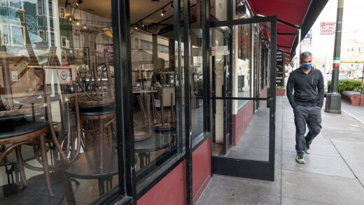 A pedestrian wearing a protective mask walks past Cafe Grecco in San Francisco, on March 17, 2020.