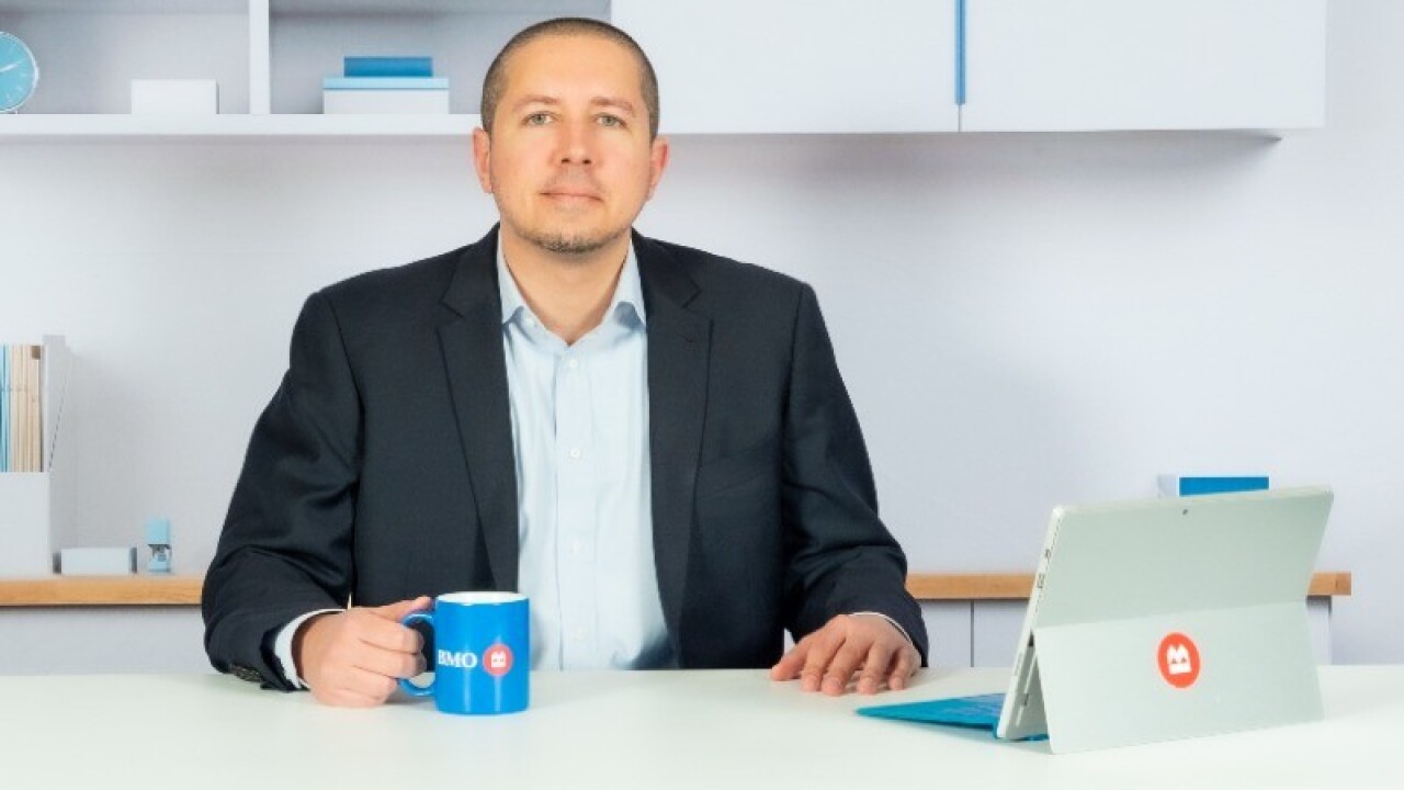 Managing director and head of enterprise social media for BMO Nicholas "Nick" Nunes sits at a desk with a BMO branded mug and tablet.