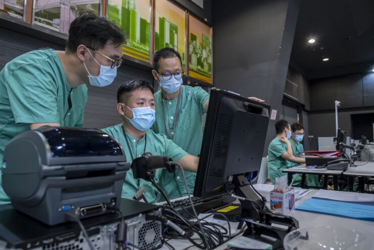 Health workers wearing protective masks look at a computer during a media tour of a temporary community treatment facility for Covid-19 patients at the AsiaWorld-Expo (AWE) in Hong Kong, China, on Saturday, Aug. 1, 2020. Hong Kong has been taken off-guard by the sudden jump of infections after managing to contain the spread locally as it tore across the world. Officials are now scrambling to slow what they're calling a third wave, while boosting health-care facilities that are reaching capacity. Photographer: Paul Yeung/Bloomberg