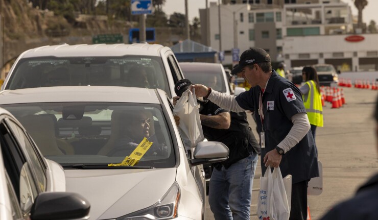 Person with Red Cross armband hands supplies to driver of car in Los Angeles