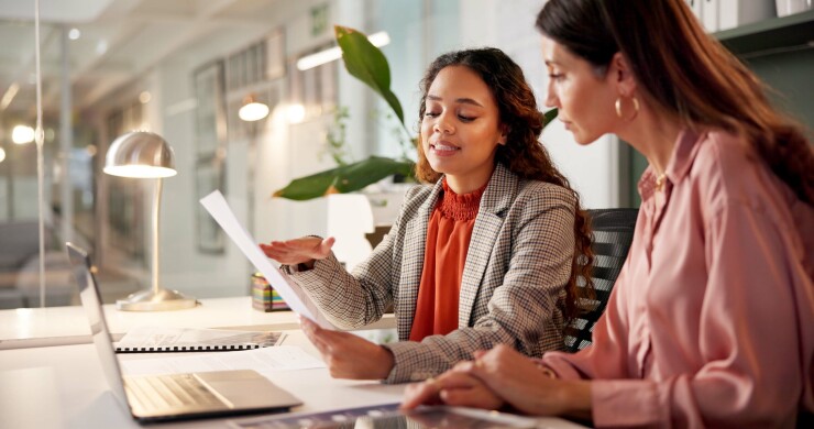 Two women talking in office, looking at paper