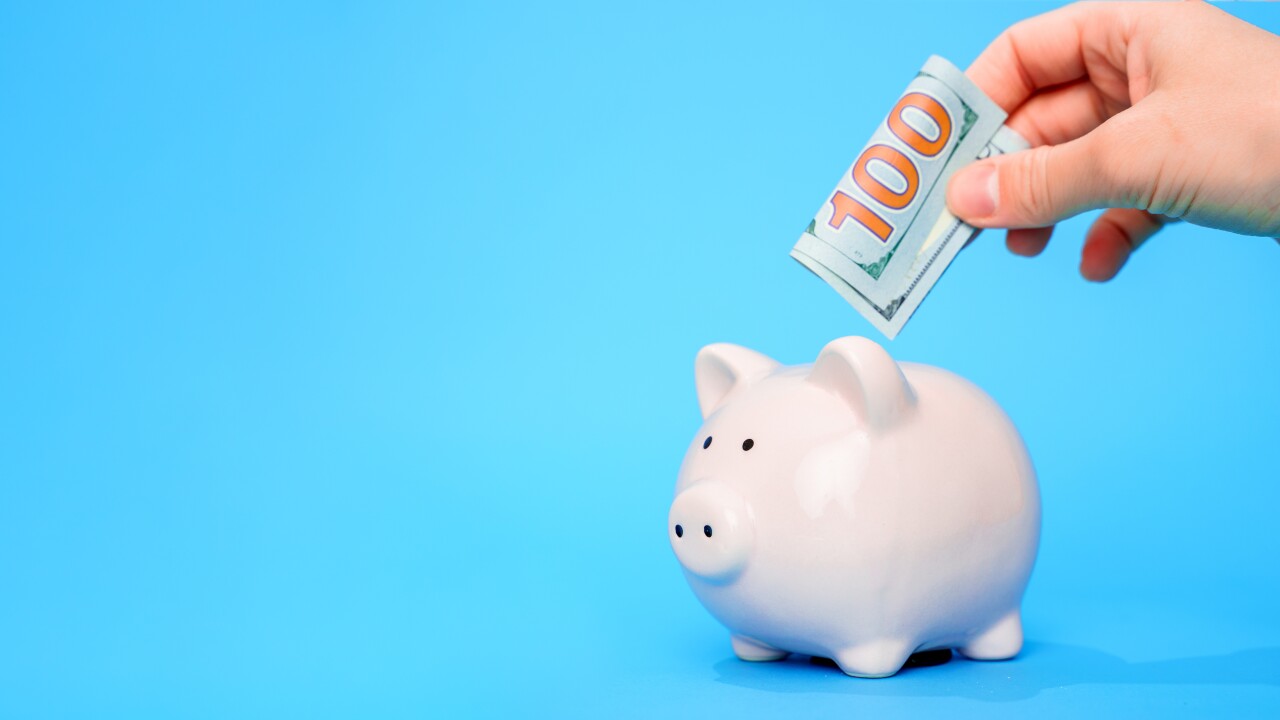 Hand putting $100 bill in piggybank