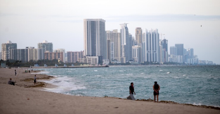 People stand on the shore in front of the skyline of Miami Beach, Florida.