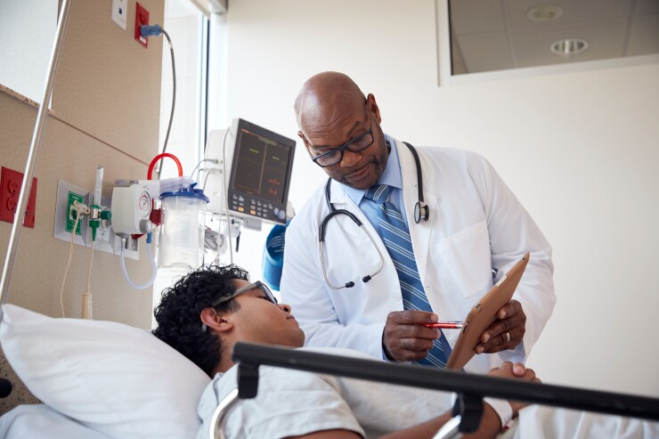 Person lying in hospital bed, doctor speaking holding tablet