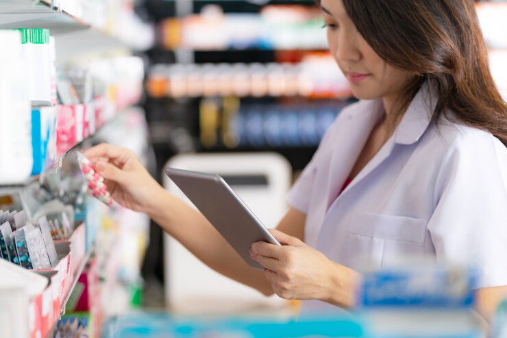 Pharmacist looking at a clip board while putting pills on a shelf