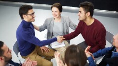 Happy men handshaking with helpful psychologist and applauding colleagues near by
