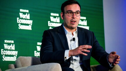 A man in a suit speaks at the Semafor World Economy Summit, gesturing with his hands against a green branded backdrop.