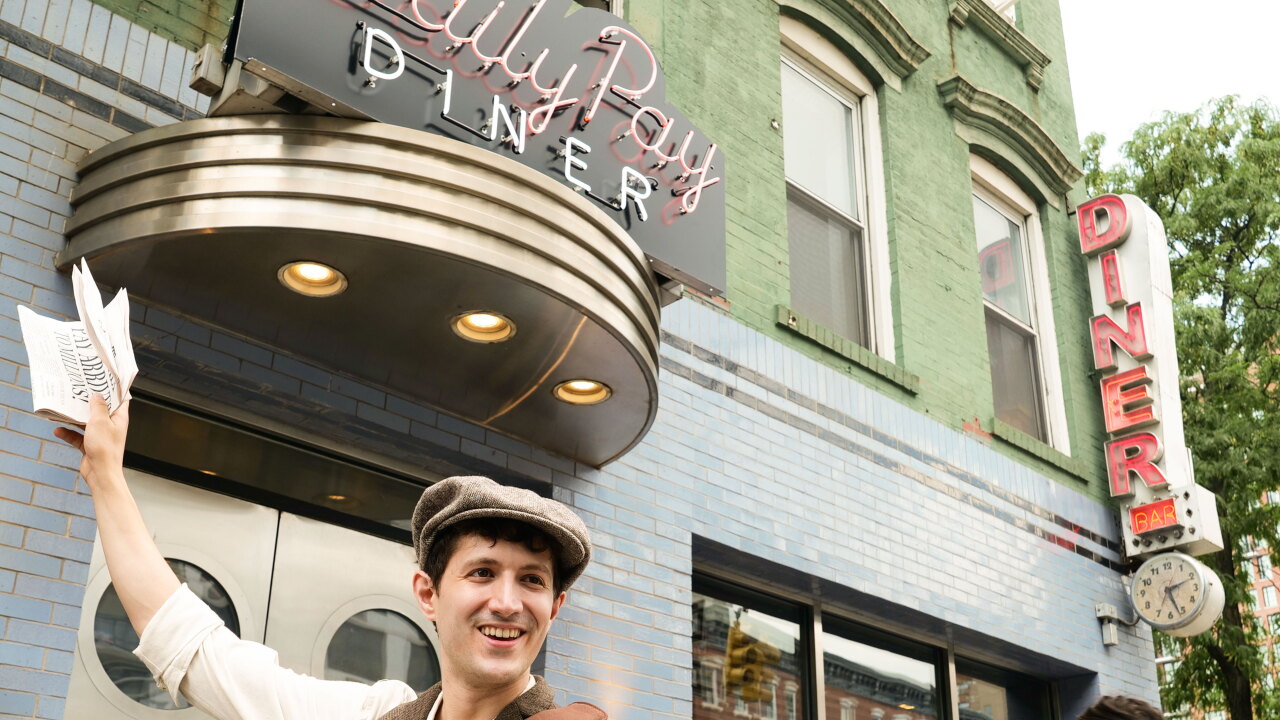 Man stands in front of a diner with a newspaper overhead.
